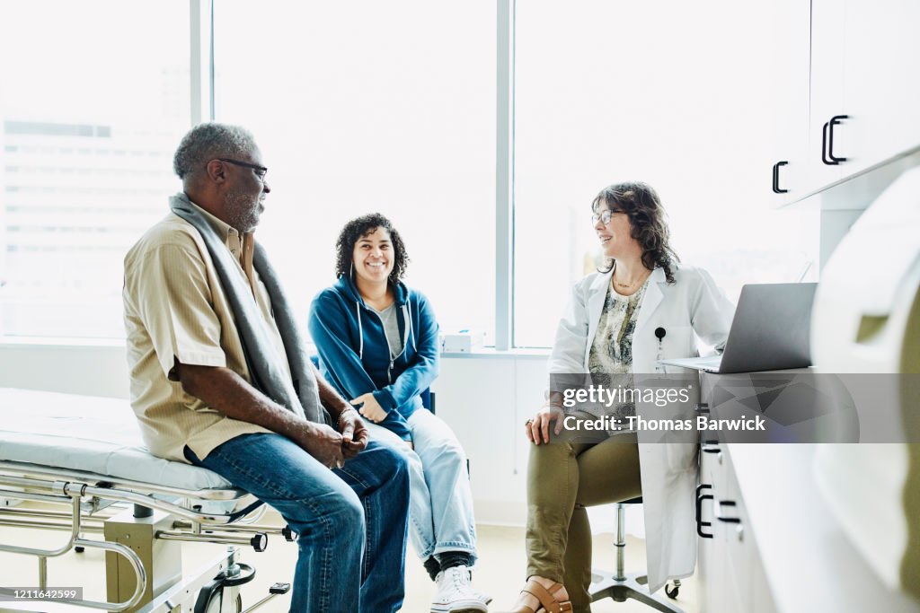 Smiling female doctor consulting with senior male patient and adult daughter in exam room