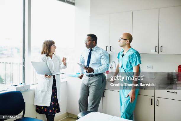 female doctor leading medical team discussion in hospital exam room - caucasian doctor and nurse using tablet computer stock-fotos und bilder