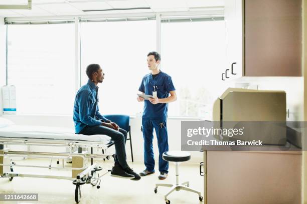 male nurse holding digital tablet while consulting with patient in exam room - nurse full length stock pictures, royalty-free photos & images