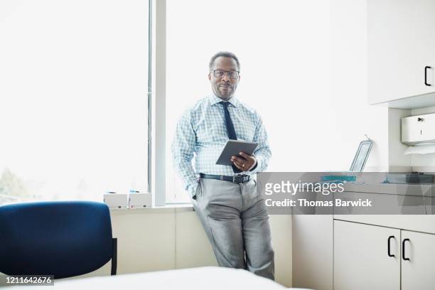 portrait of doctor holding digital tablet in exam room - doctor attitude stock pictures, royalty-free photos & images