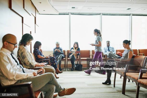 nurse walking through medical office waiting room to greet patient - doctors office stock-fotos und bilder