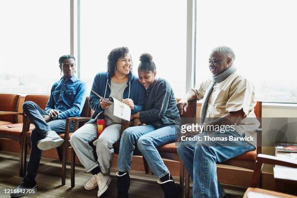 smiling family reading magazine while sitting in hospital waiting room - treats magazine stock-fotos und bilder