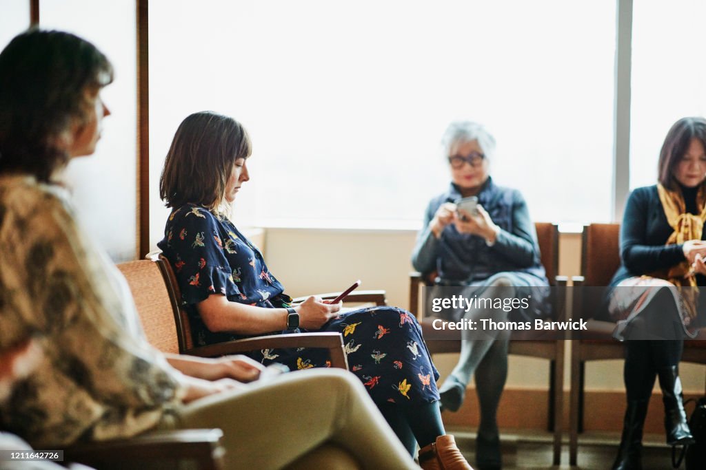 Woman looking at smart phone while sitting in medical office waiting room