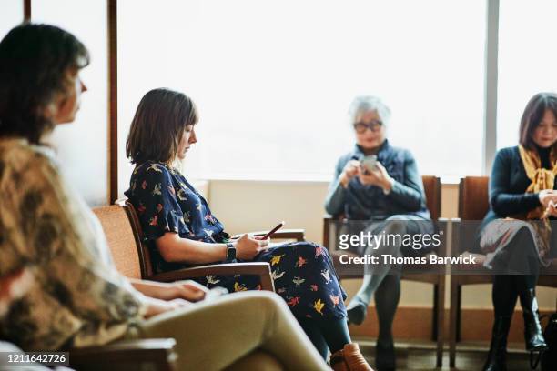 woman looking at smart phone while sitting in medical office waiting room - väntrum bildbanksfoton och bilder
