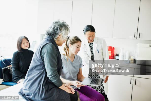 female doctor and nurse showing senior female patient information on laptop during medical exam - group people thinking stock pictures, royalty-free photos & images