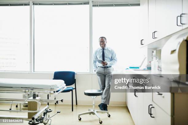 portrait of laughing doctor holding digital tablet in exam room - medical examination room stock pictures, royalty-free photos & images