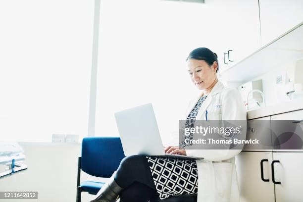 portrait of female doctor working on laptop in exam room - doctor on computer stock pictures, royalty-free photos & images