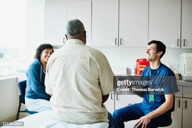 senior male patient and adult daughter laughing with male nurse during check up in exam room - family hospital old stock-fotos und bilder