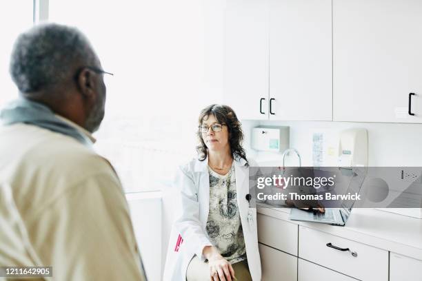 smiling female doctor consulting with senior male patient in exam room - patient room stockfoto's en -beelden