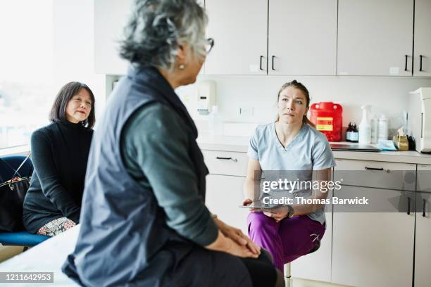 nurse listening to senior female patient during consultation in exam room - premium access images stock pictures, royalty-free photos & images