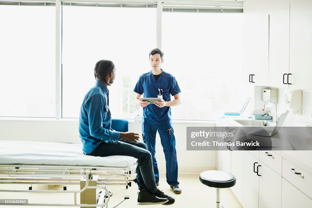 Male nurse holding digital tablet while in discussion with patient in exam room