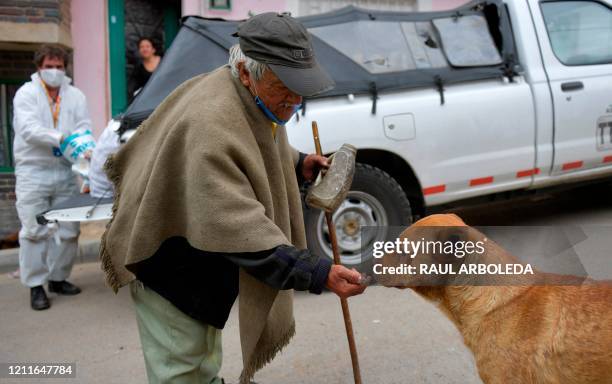 An elderly man feeds a dog after the arrival of donated food in Ciudad Bolivar neighbourhood, southern Bogota, on May 2, 2020. - La Ruta Animal is a...