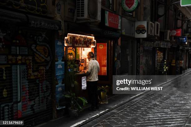 Man orders from a cafe in a small deserted laneway usually packed with open cafes and people during their lunchtime in Melbourne on May 4, 2020.