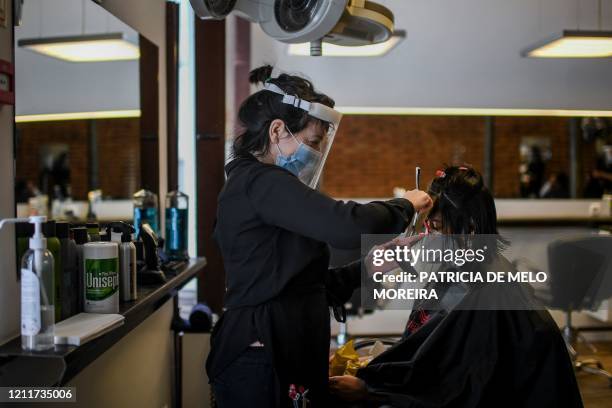 Portuguese hair stylist Silvia Pereira wearing a face mask and a shield cuts the hair of a costumer at a hair salon in Lisbon on May 4, 2020 as...