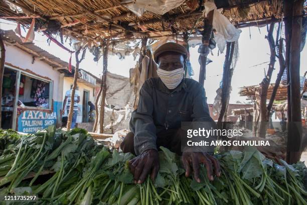 Vegetable vendor displays his products while wearing a face mask made by Tayamba Tailoring shop seen left, inside the Area 23 agricultural commodity...