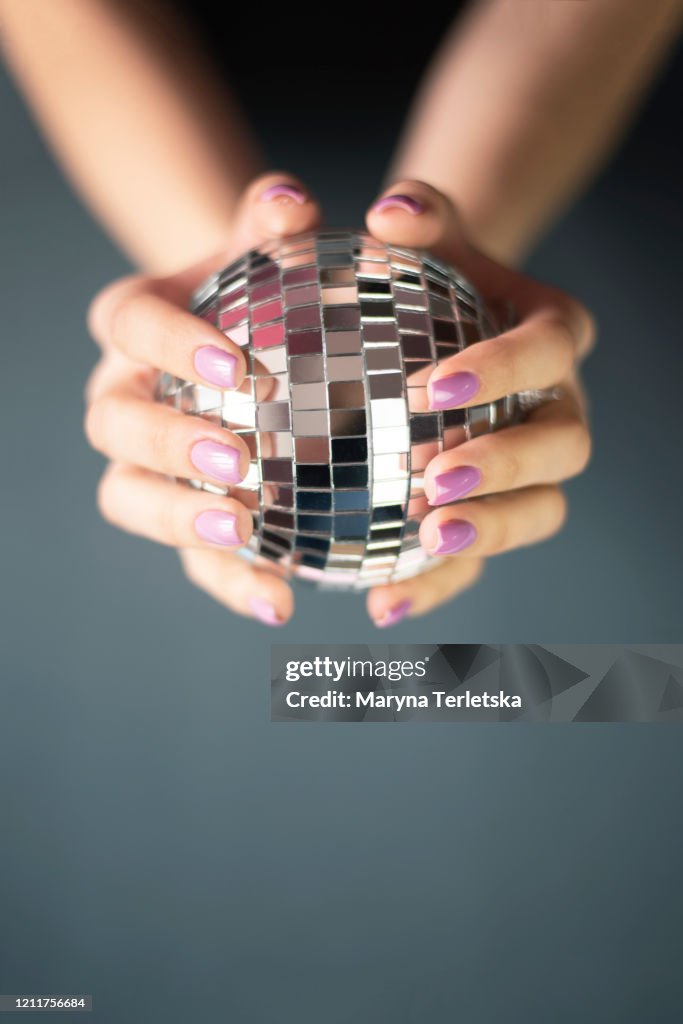 Female hands with manicure hold a disco ball.
