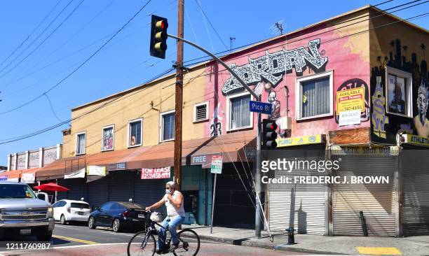 Man adjusts his facemask riding past closed shopfronts in what would be a normally busy fashion district in Los Angeles, California on May 4, 2020. -...