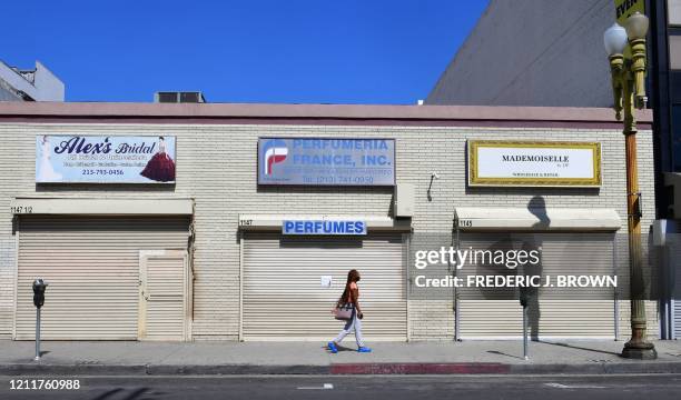 Woman walks past closed shopfronts in what would be a normally busy fashion district in Los Angeles, California on May 4, 2020. - California governor...