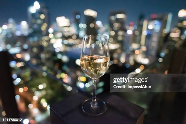 close up view of white wine glass at the rooftop bar with blur bokeh lights at night - rooftop at night bildbanksfoton och bilder