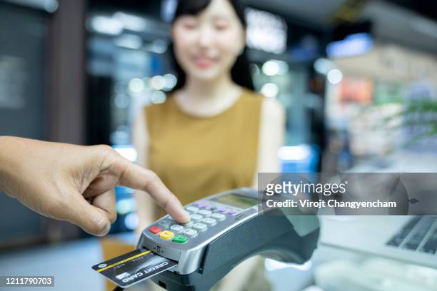 asian female paying for her purchase by credit card with reader machine - debit cards, credit cards accepted stockfoto's en -beelden