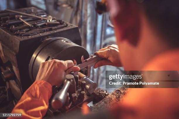 worker handles metal at lathe turner measures the dimensions of the metal workpiece with a caliper in uniform with safety. work on a lathe. - compasso de calibre imagens e fotografias de stock