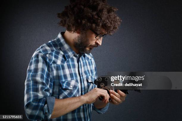 young cinematographer adjusting his old fashioned film camera before shooting a scene with it - cameraman grey background stock pictures, royalty-free photos & images