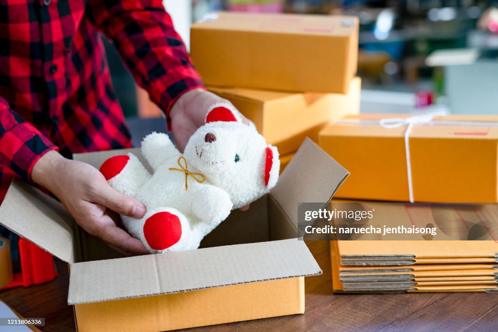 A young man starts a small business owner packing a teddy bear in a box at work. Independent male seller prepares products for the packing process at home Online sales internet marketing e-commerce concept