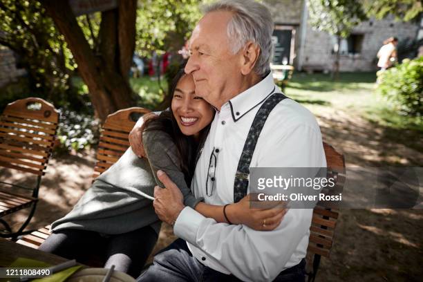 happy young woman embracing senior man at garden table - old man young woman fotografías e imágenes de stock