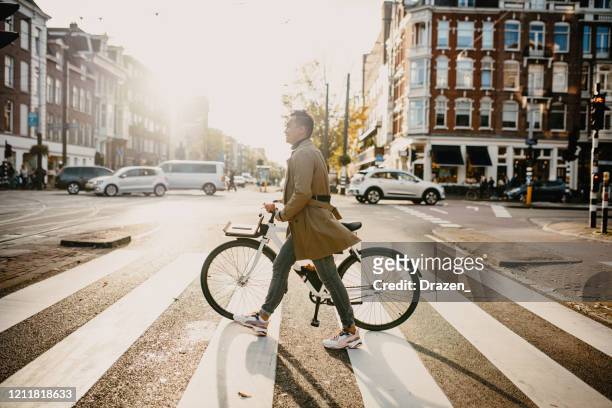 millennial japanese commuter in the city with bicycle, crossing the street - netherlands stock pictures, royalty-free photos & images