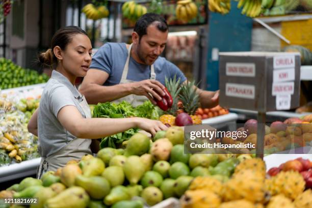 team of vendors at a market stall preparing a delivery for customer in a carton box while talking and smiling - market square stock pictures, royalty-free photos & images