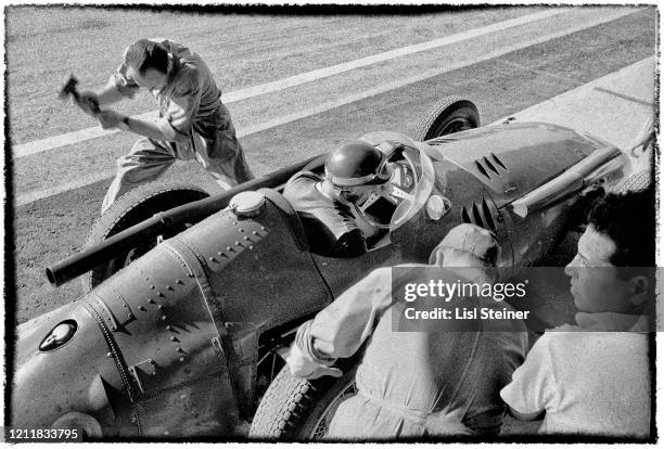 Elevated view of Argentine racecar driver Juan Manuel Fangio in his Maserati 250F, surrounded by his crew, during a pit stop in the Buenos Aires...