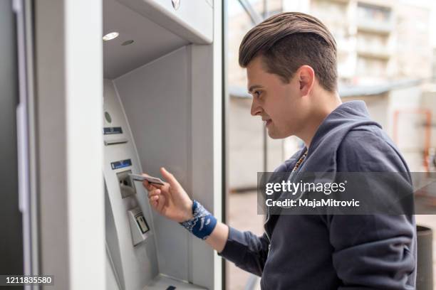 man using his credit card in an atm for cash withdrawal - man atm smile stock pictures, royalty-free photos & images