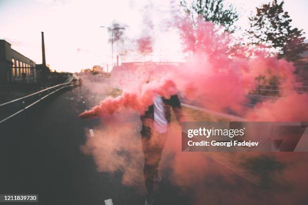 man in a leather jacket standing at the street with smoke bomb. colorful portrait of european teenager with red smoke bomb. - urban warfare stock pictures, royalty-free photos & images