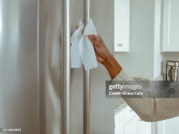 woman cleans refrigerator handle using disinfectant wipe - rvs stockfoto's en -beelden