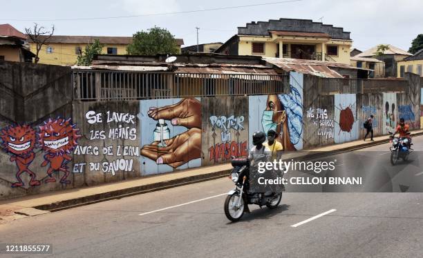 Residents on motorcycles drive past graffiti on a wall depicting hygiene measures to curb the spread of the COVID-19 coronavirus in Conakry, Guinea,...