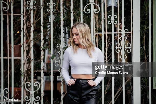 blond girl in white crop top and leather pants against ornate white gate - leather pants stock-fotos und bilder