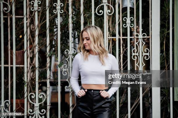 blond girl in white crop top and leather pants against ornate white gate - pantalón decorado fotografías e imágenes de stock