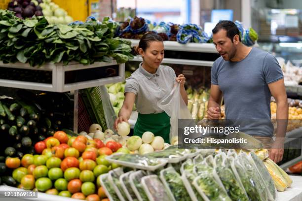 latijns-amerikaanse verkoper die mannelijke klant helpt zijn groenten te kiezen terwijl het toevoegen van hen aan een plastic zak - marktplein stockfoto's en -beelden