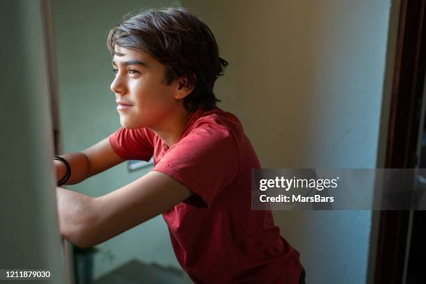 hopeful latinx preadolescent boy looking out through window, reflecting, - 12 year old cute boys stock pictures, royalty-free photos & images