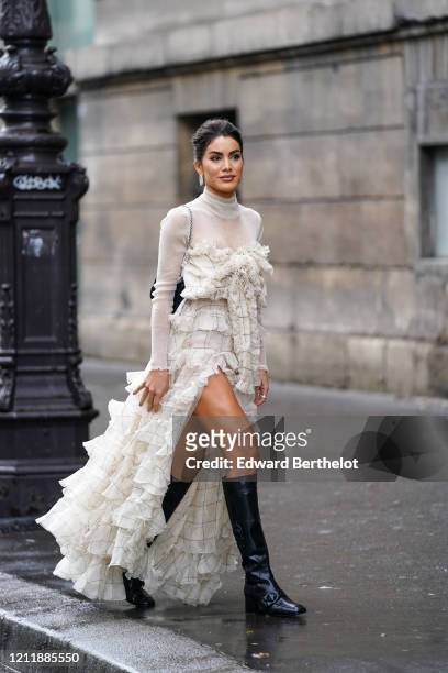 Camila Coelho wears earrings, a hi-neck glittering white lame top, a white and black window-pane patterned front-split, frilly and ruffled long...