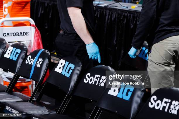 Trainers wear rubber gloves as they work in the bench area during the first round of the Big Ten Men's Basketball Tournament game between the...