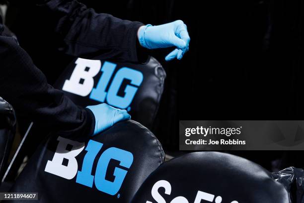 Trainers wear rubber gloves as they work in the bench area during the first round of the Big Ten Men's Basketball Tournament game between the...