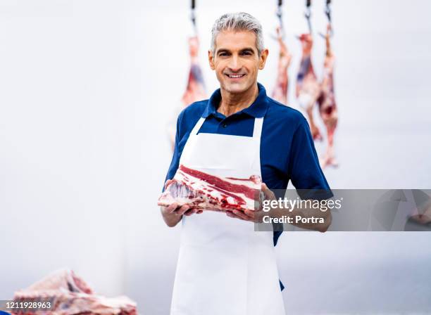 carnicero confiado sosteniendo carne fresca cruda - carnicero fotografías e imágenes de stock