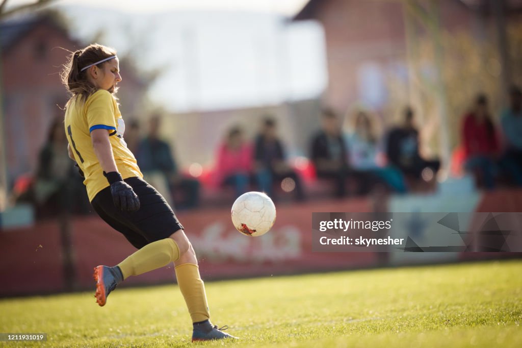 Full längd av kvinnlig målvakt sparkar fotboll på spelplanen.