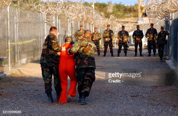 In this photo released 18 January 2002 by the Department of Defense, U.S. Army military police escort a detainee to his cell in Camp X-Ray at the US...
