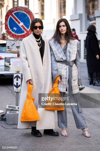 Allegra Benini , wearing a long cream coat, orange bag and black boots, and Chiara Totire , wearing a grey checked suit, light grey checked vest,...