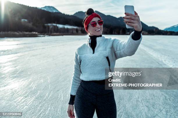 a woman taking a moment to snap a selfie of herself using a smart phone while ice skating on a frozen lake - figure skater stock pictures, royalty-free photos & images