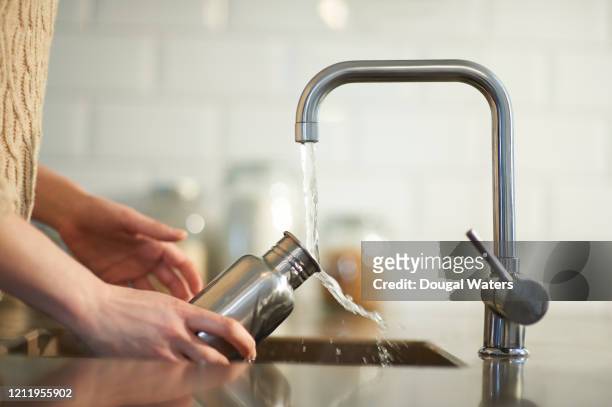 cleaning a plastic free reusable water bottle in kitchen sink. - water photos et images de collection