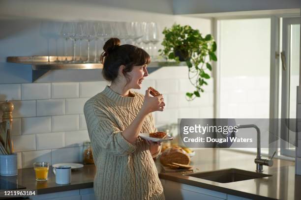 woman eating toast at breakfast and looking out of kitchen window. - torrada - fotografias e filmes do acervo