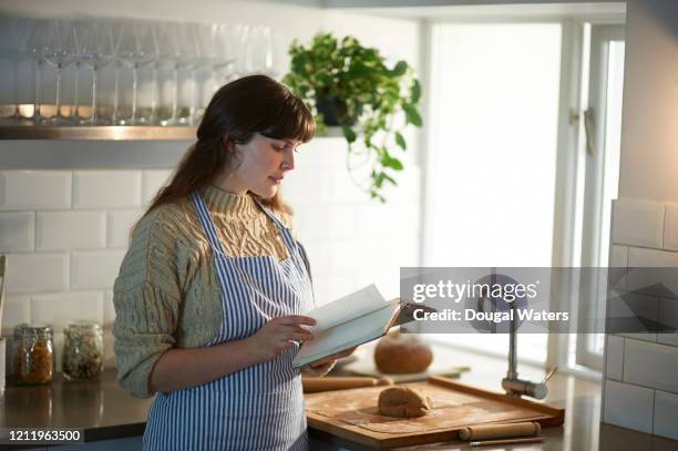 woman making pastry in kitchen reading recipe book. - kochbuch stock-fotos und bilder